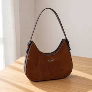 Brown McLANEE hobo shoulder bag with dark trim and a curved silhouette displayed on a sunlit wooden table.