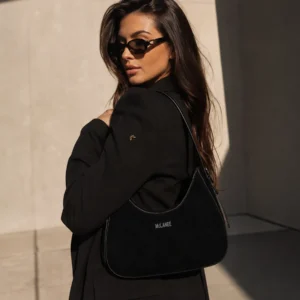 Woman wearing a black McLANEE Elysia leather hobo bag with a curved silhouette and shoulder strap, styled with a black blazer.